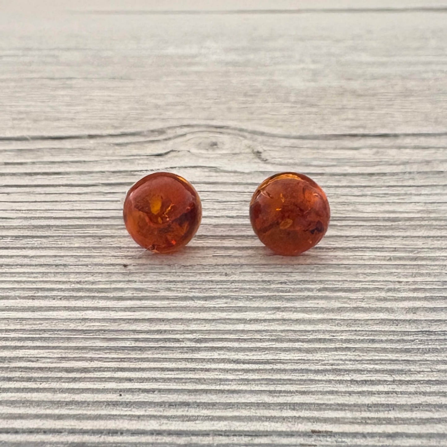 Pair of amber-colored round stud earrings on a wooden surface