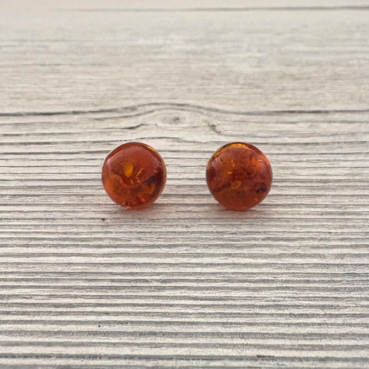 Pair of amber-colored round stud earrings on a wooden surface