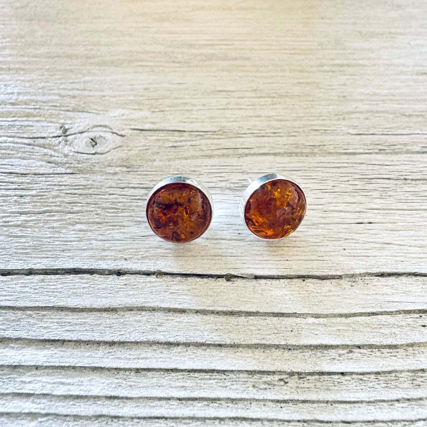 A pair of round stud earrings with amber-colored inlay in a silver bezel setting.
