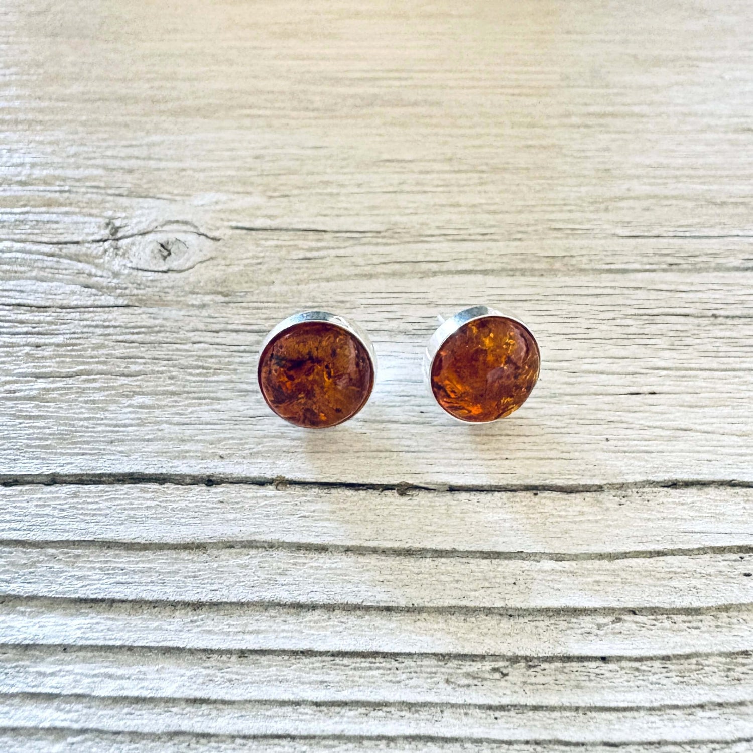 A pair of round stud earrings with amber-colored inlay in a silver bezel setting.