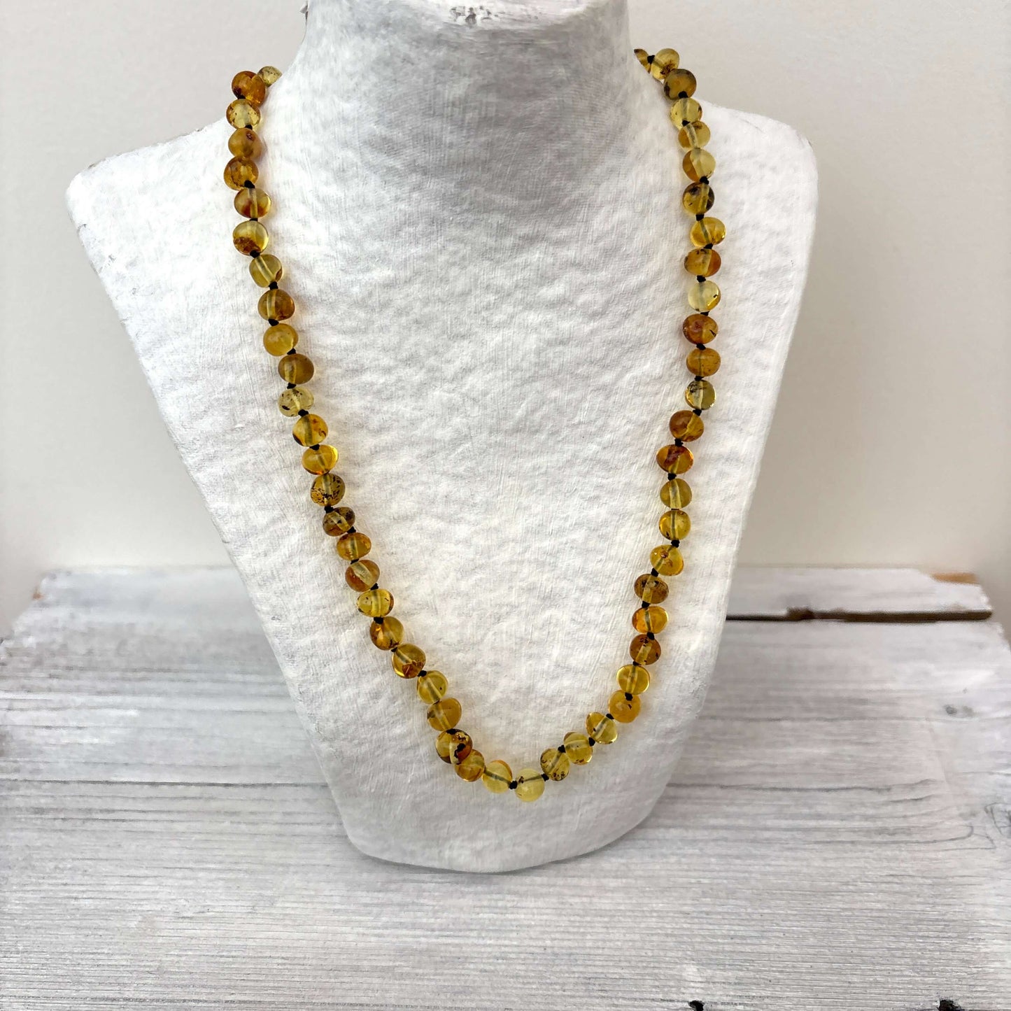 Amber necklace with light green beads on a white mannequin bust against a light background