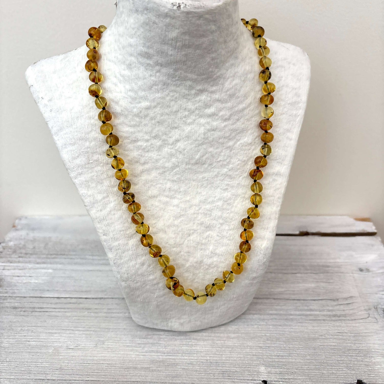Amber necklace with light green beads on a white mannequin bust against a light background