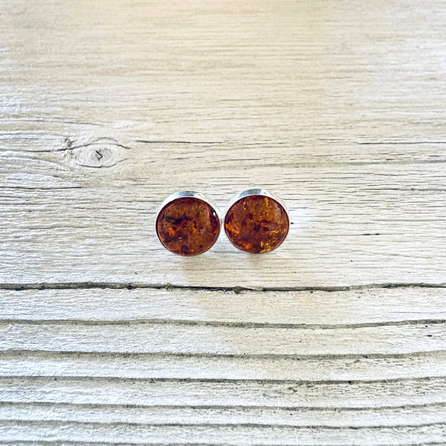 Round cognac Baltic amber stud earrings with a polished silver bezel setting.