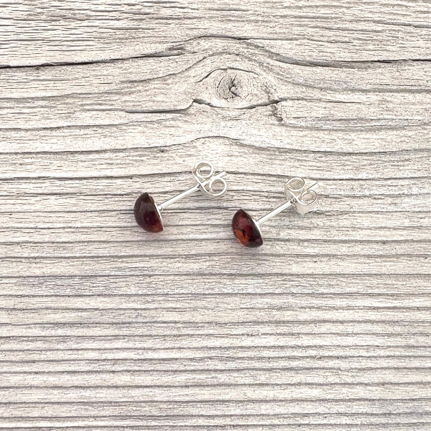 Pair of silver stud earrings with red gemstones on a wooden surface