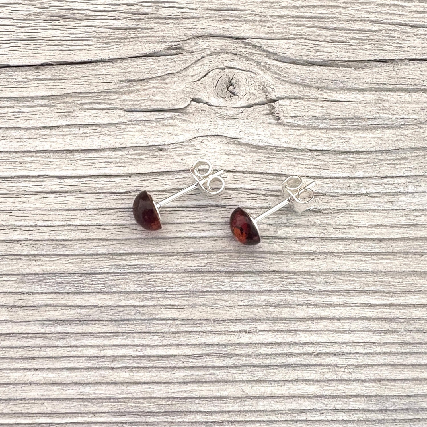 Pair of silver stud earrings with red gemstones on a wooden surface
