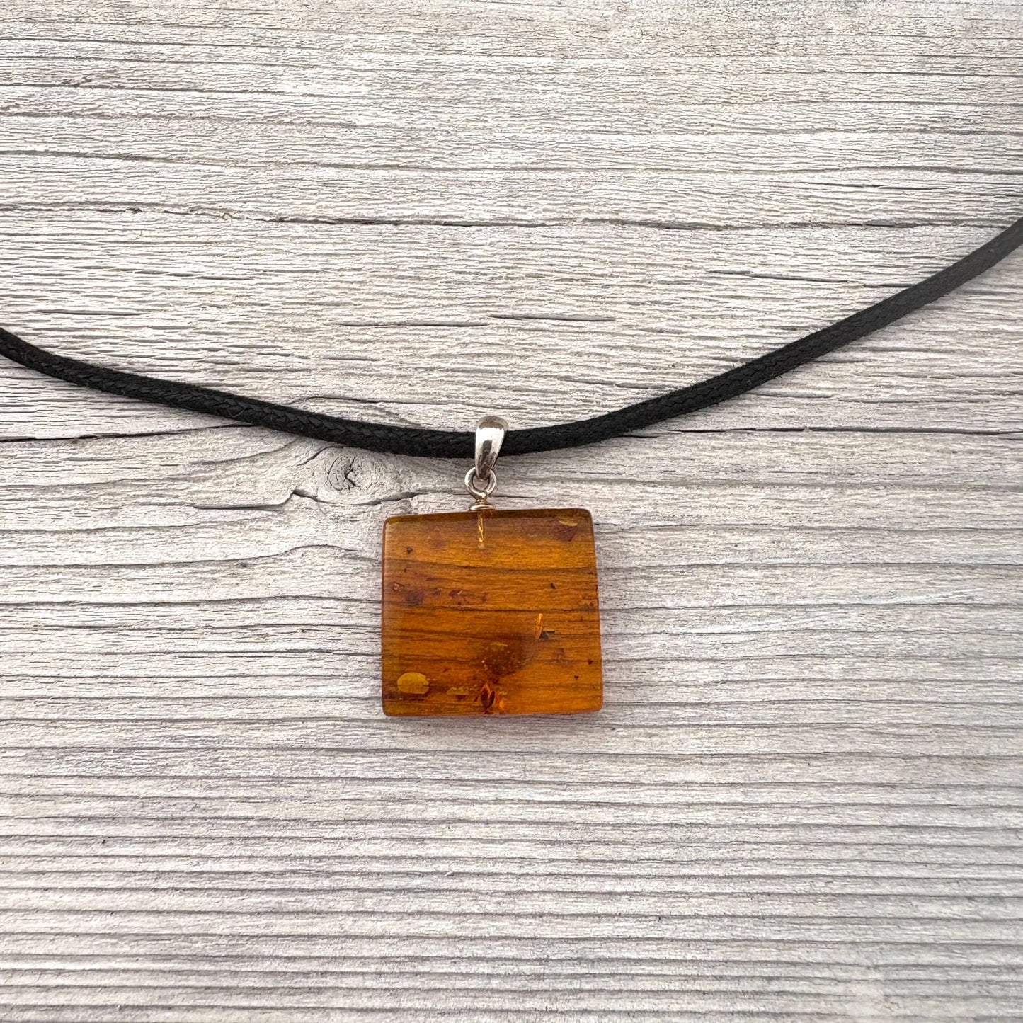 Square amber pendant on a black cord against a gray wooden background