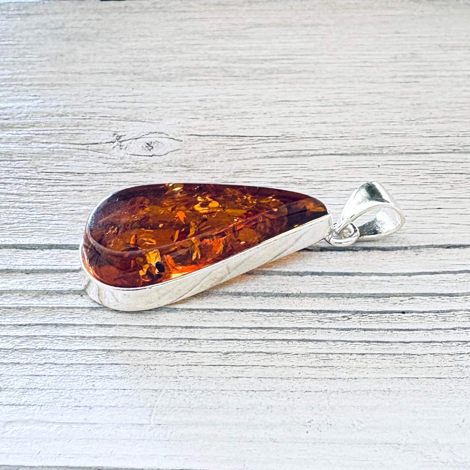 Large cognac Baltic amber teardrop pendant featuring visible natural inclusions, and a polished silver bail