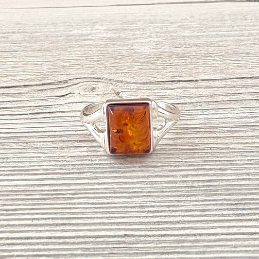 Silver ring with a rectangular amber stone on a wooden surface