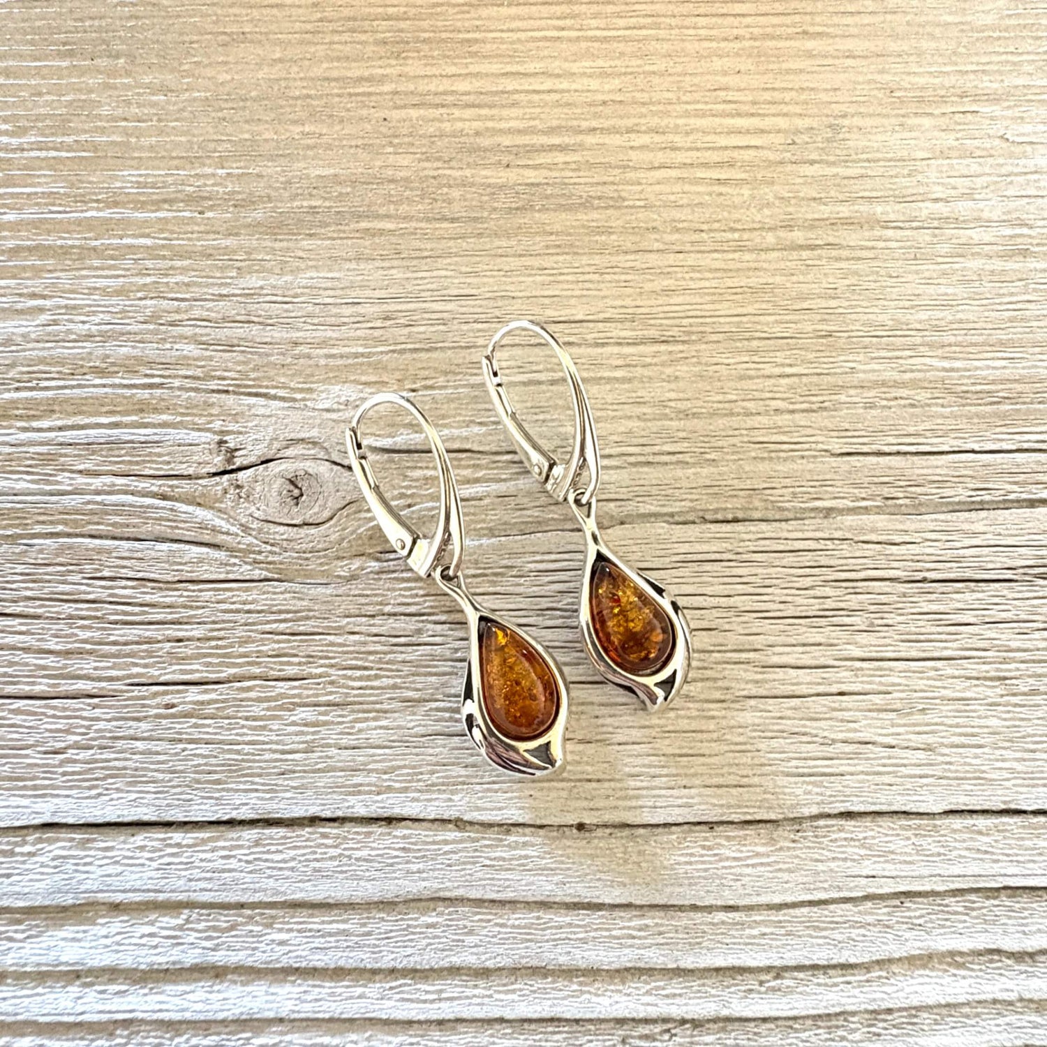 A pair of silver leverback earrings with teardrop-shaped amber gemstones, displayed on a light-colored wooden surface.