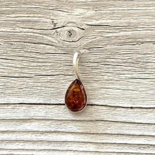 Teardrop shaped amber pendant against a wooden background